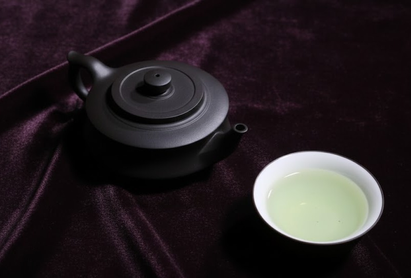 Black teapot with gyokuro tea on purple background